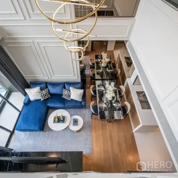 Condominium for rent in Khlong Toei, Bangkok - Overhead view of a double-height living and dining area with a blue sofa, marble dining table, wood floors and a modern gold chandelier.