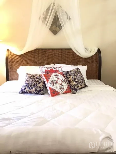 Detached House for rent in Phra Khanong, Bangkok - Bedroom with a rattan headboard, white bedding, and patterned accent pillows.