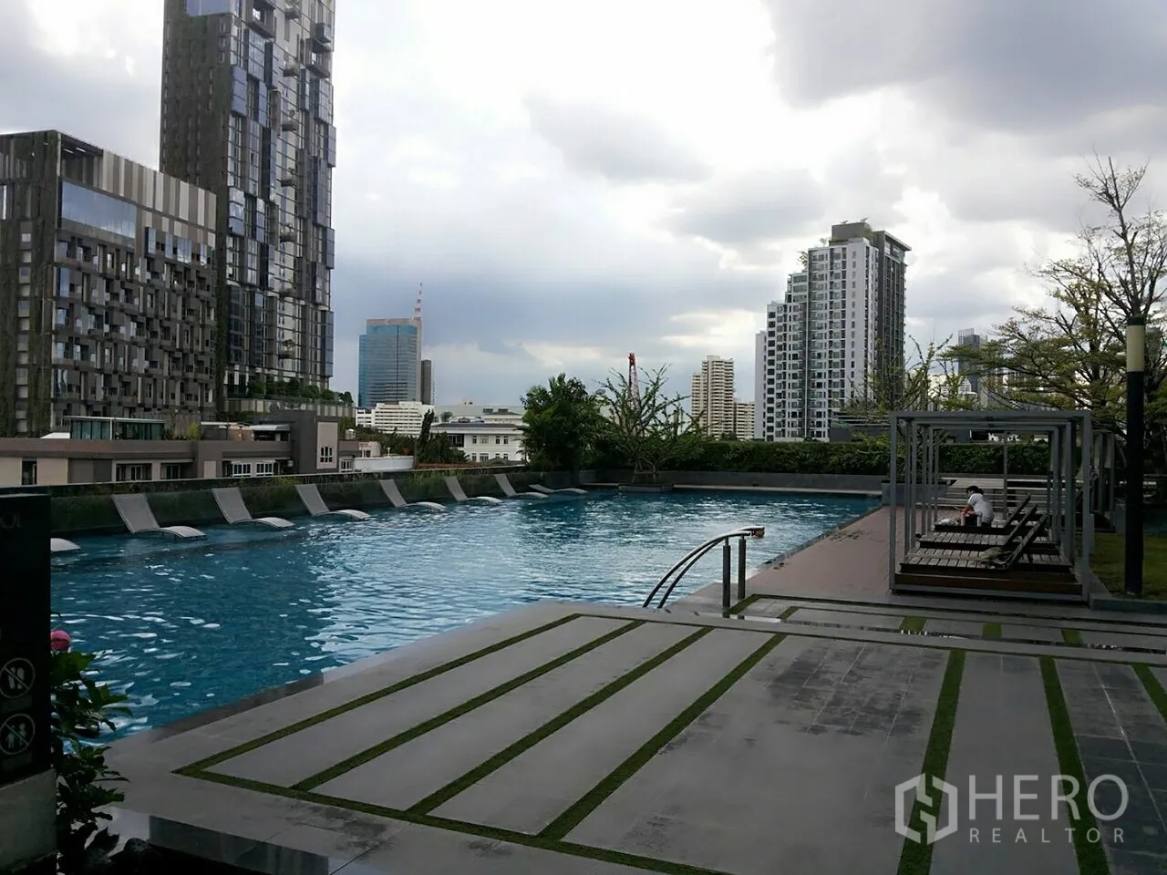 Condominium for rent in Khlong Toei, Bangkok - Outdoor swimming pool with sun loungers and city buildings in the background.