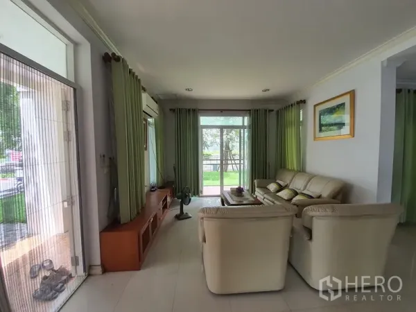独立式住宅 出租在Lat Krabang, Bangkok - 明亮客厅，奶油色沙发、内置电视柜，落地滑门通向花园。