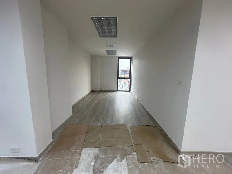 Office Space for rent - Long private office or meeting room with wood floors, ceiling vents, and a window at the end providing daylight.