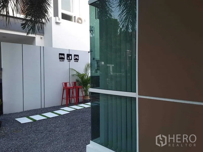 Detached House for rent in Lam Luk Ka, Pathum Thani - Side yard with gravel path, tall window and red bar stools by a privacy wall.