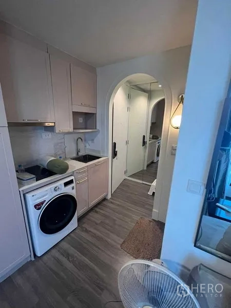 公寓 出售在Ratchathewi, Bangkok - 现代小厨房，水槽与橱柜，前置洗衣机，通向拱形走廊与镜面衣柜。
