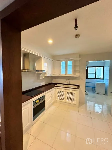 Condominium for rent in Bangkok - U-shaped kitchen with white cabinets, oven, cooktop and sink.