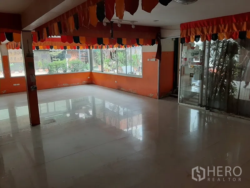 Retail Space for rent in Watthana, Bangkok - Corner retail hall with large wraparound windows, orange accent walls and glossy tile flooring.