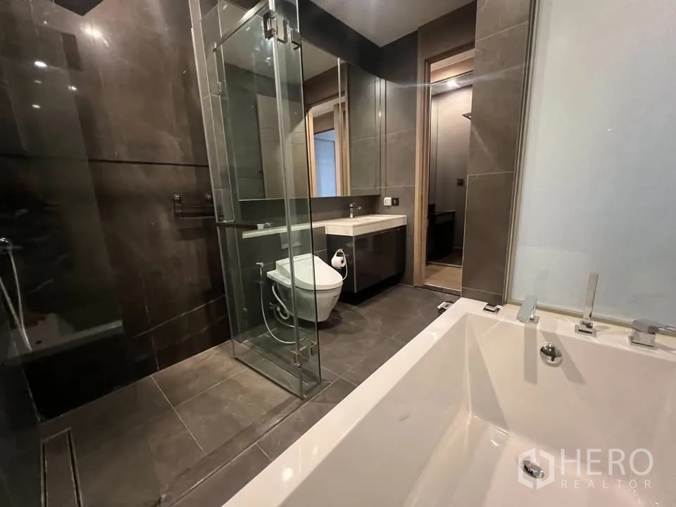 公寓 出租在Huai Khwang, Bangkok - 卫浴采用深色瓷砖，玻璃淋浴间与前景浴缸边。