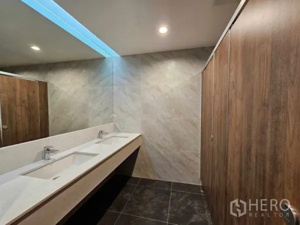Office Space for rent in Bang Rak, Bangkok - Modern restroom with twin sinks, stone tiles and wood-finish partitions.