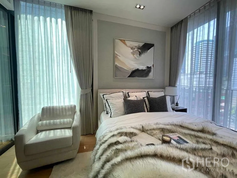 Condominium for rent in Pathum Wan, Bangkok - Primary bedroom with corner windows, city view and a comfortable armchair.