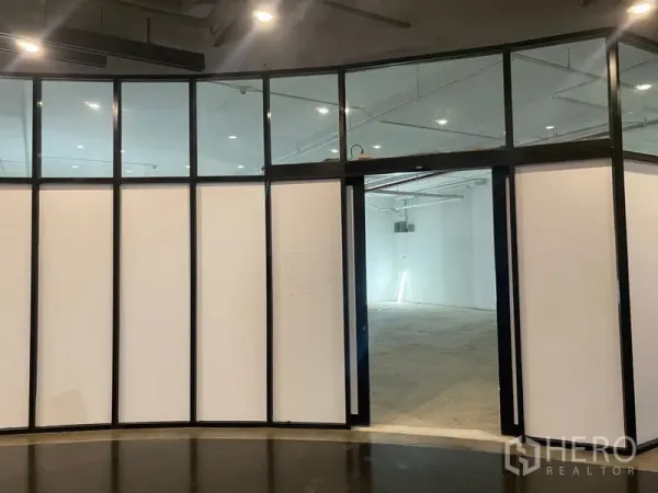 Retail Space for rent - Curved black‑framed glass storefront opening to a white‑shell retail unit with ceiling spotlights.