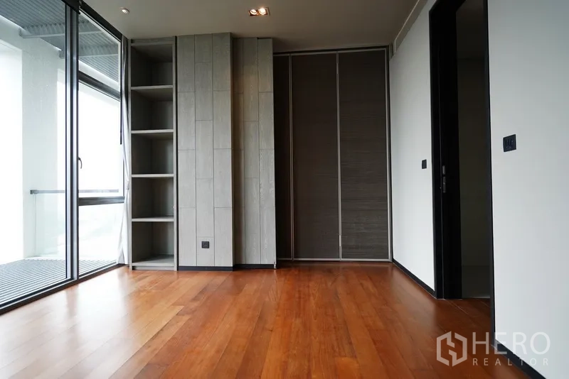 Condominium for rent in Sathon, Bangkok - Bedroom with balcony access, built-in shelving, large wardrobe and wooden floors.