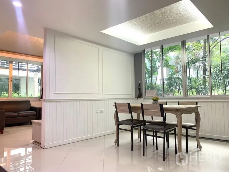 Condominium for rent in Khlong Toei, Bangkok - Dining area with wooden table, ceiling light and large windows facing lush garden view.