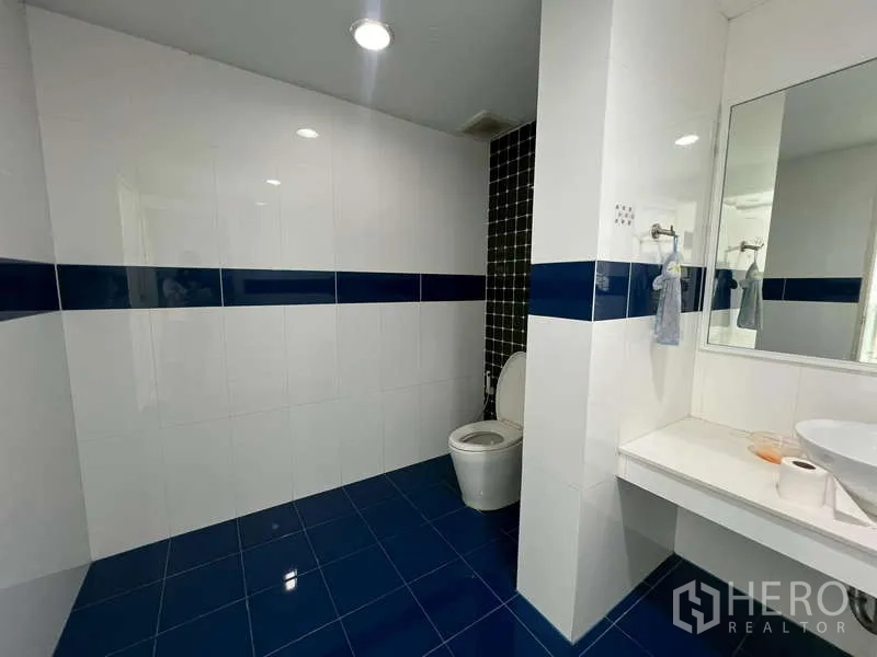 Showroom for rent - Clean restroom featuring white tiles, blue accents, and a wall mirror.