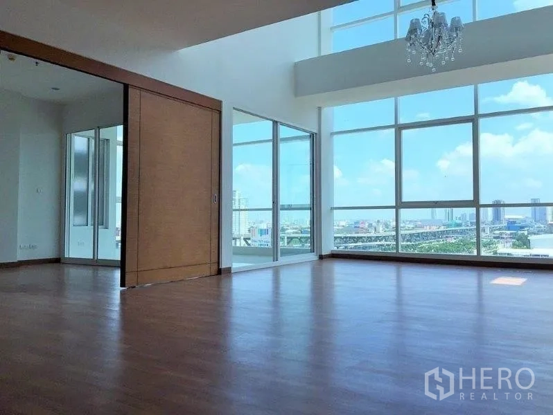 Condominium for sale in Bang Na, Bangkok - Spacious double-height living room with chandelier, wood floors and skyline views through large picture windows.