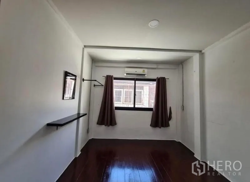 Townhouse for rent in Chatuchak, Bangkok - Simple bedroom with window, air conditioner and dark wood flooring.