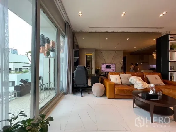 Condominium for rent in Pathum Wan, Bangkok - Sliding glass doors open to terrace beside study nook and tan sofa in open-plan lounge.