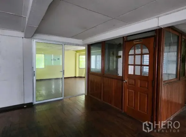 Retail Space for rent in Bang Rak, Bangkok - Interior corridor with dark wood floors, a glass-partitioned office and arched wooden manager door beside a sliding glass entry to a bright room.