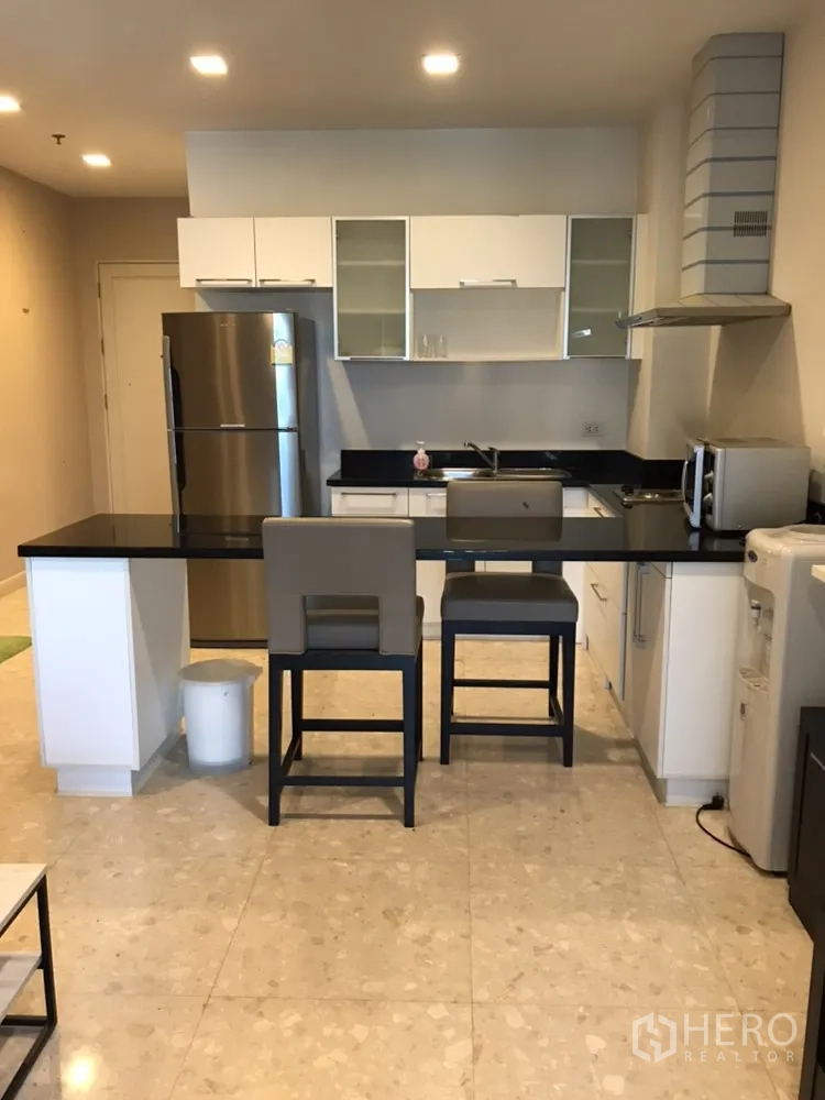 Condominium for rent in Khlong Toei, Bangkok - Modern kitchen with black countertops, white cabinets, breakfast bar and stainless appliances.