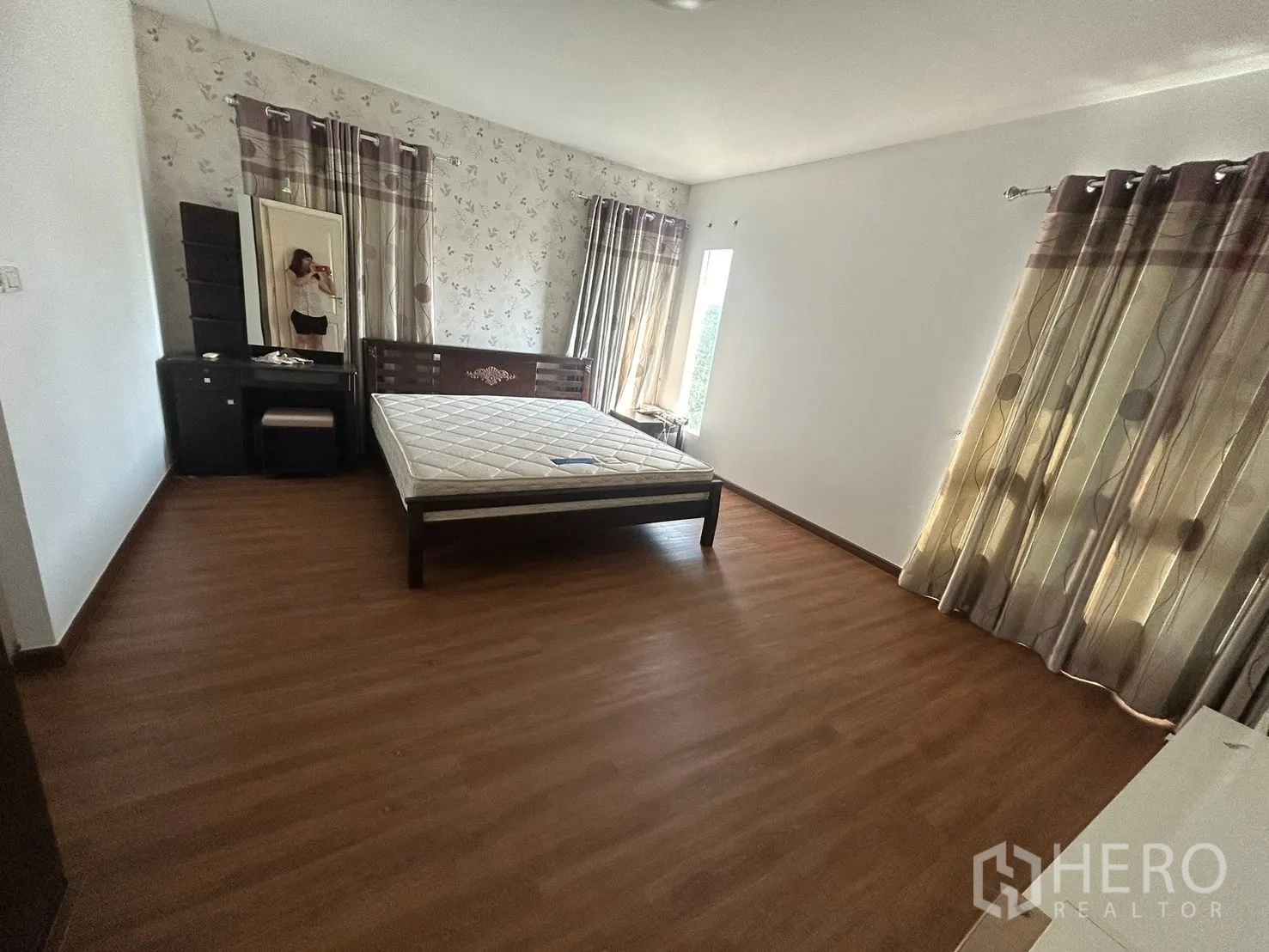 Detached House for rent in Bang Na, Bangkok - Spacious bedroom with wood flooring, bed frame, vanity, and large windows.