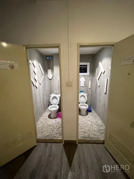 Shophouse for rent or sale in Watthana, Bangkok - Two separate toilet stalls with grey finishes and pebble‑stone flooring.