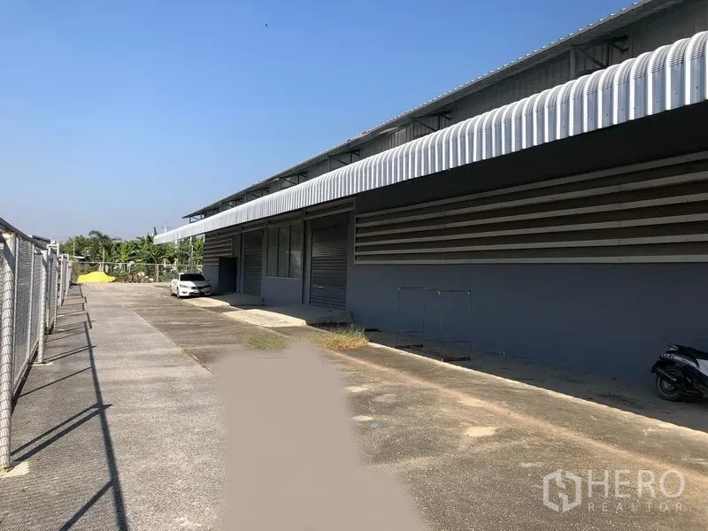 Factory for rent in Bang Bua Thong, Nonthaburi - Long exterior facade featuring covered loading dock, roller shutters, and wide driveway.
