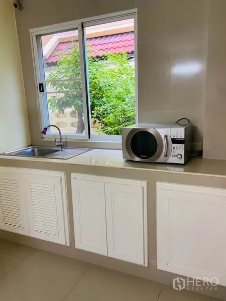 Detached House for rent in Watthana, Bangkok - Kitchen counter with sink, window, microwave and storage cabinets.