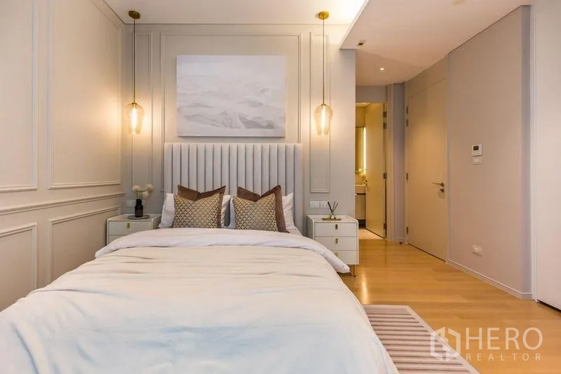 Condominium for rent in Pathum Wan, Bangkok - Bedroom with soft lighting, panelled walls, and entrance to an ensuite bathroom.