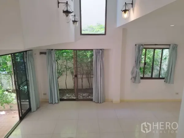 Detached House for rent in Watthana, Bangkok - Double-height living area with tall windows and sliding doors to a small garden.