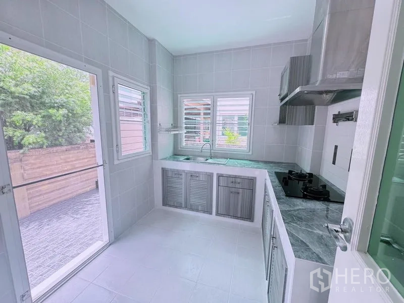 บ้าน ให้เช่าในPrawet, Bangkok - ห้องครัวปูกระเบื้องสว่าง เคาน์เตอร์รูปตัวแอล เตาแก๊ส เครื่องดูดควัน พร้อมหน้าต่างและประตูออกลาน