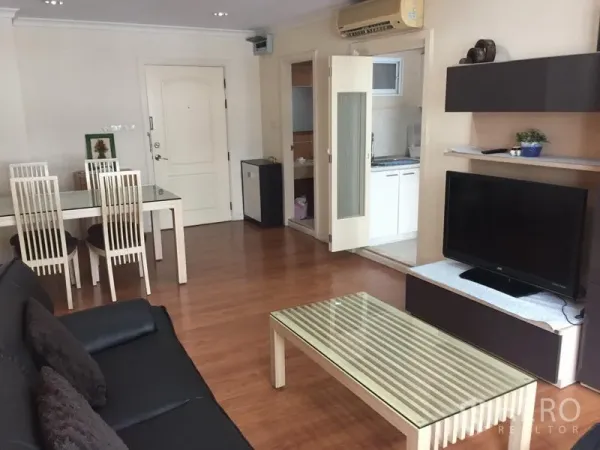 Condominium for rent in Watthana, Bangkok - Open-plan living and dining area with wood flooring, sofa, TV console and a glass-top table.