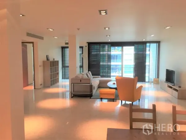 Condominium for rent in Khlong Toei, Bangkok - Bright lounge with floor-to-ceiling windows, blinds and a TV unit creating a spacious living space.