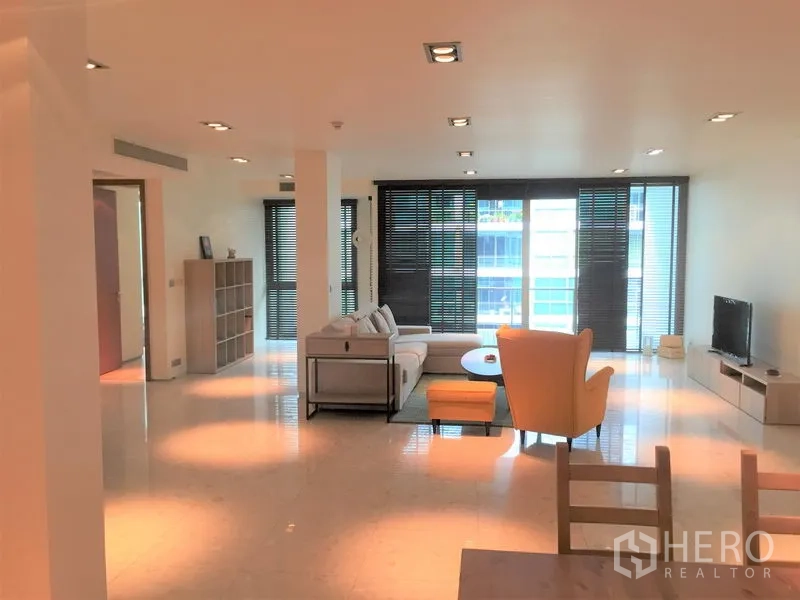 Condominium for rent in Khlong Toei, Bangkok - Bright lounge with floor-to-ceiling windows, blinds and a TV unit creating a spacious living space.