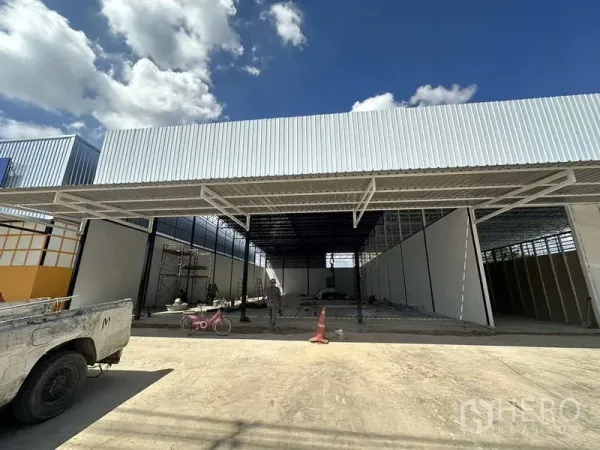 Warehouse for rent in Lam Luk Ka, Pathum Thani - Front view of a new steel-frame warehouse with a wide covered loading bay and concrete yard under a blue sky