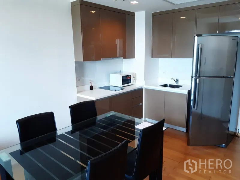 Condominium for rent in Khlong Toei, Bangkok - Modern corner kitchen with glossy cabinets, glass dining table and stainless-steel fridge