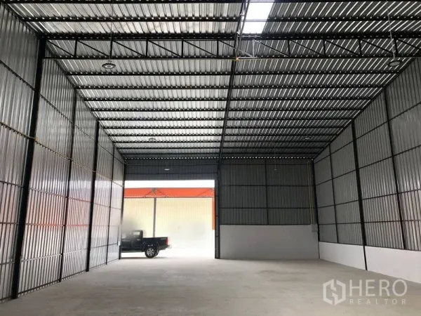 Warehouse for rent in Pathum Thani - Open-plan warehouse facing a large sliding door with a pickup truck at the loading bay.