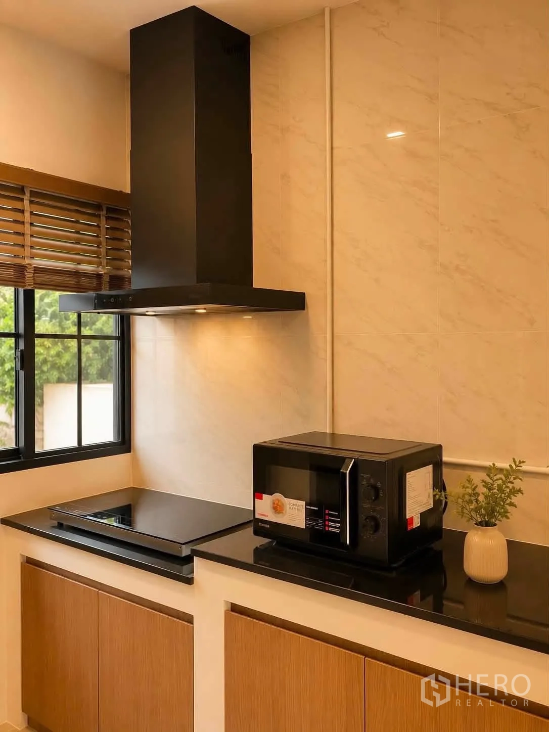 Detached House for rent in Bang Phli, Samut Prakan - Modern kitchen with black countertop, window, cooktop, hood and microwave.