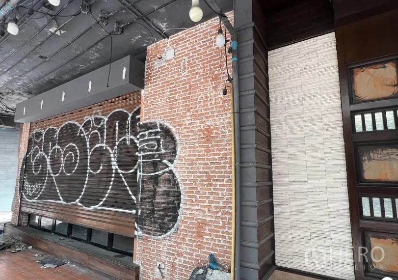 Shophouse for rent in Khlong Toei, Bangkok - Close-up of brick exterior wall with roller shutter and exposed ceiling fixtures along the storefront.