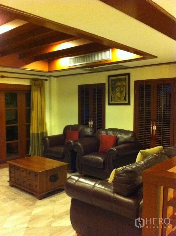 Townhouse for rent or sale in Watthana, Bangkok - Warm living room with leather sofas, wooden ceiling beams and sliding doors.
