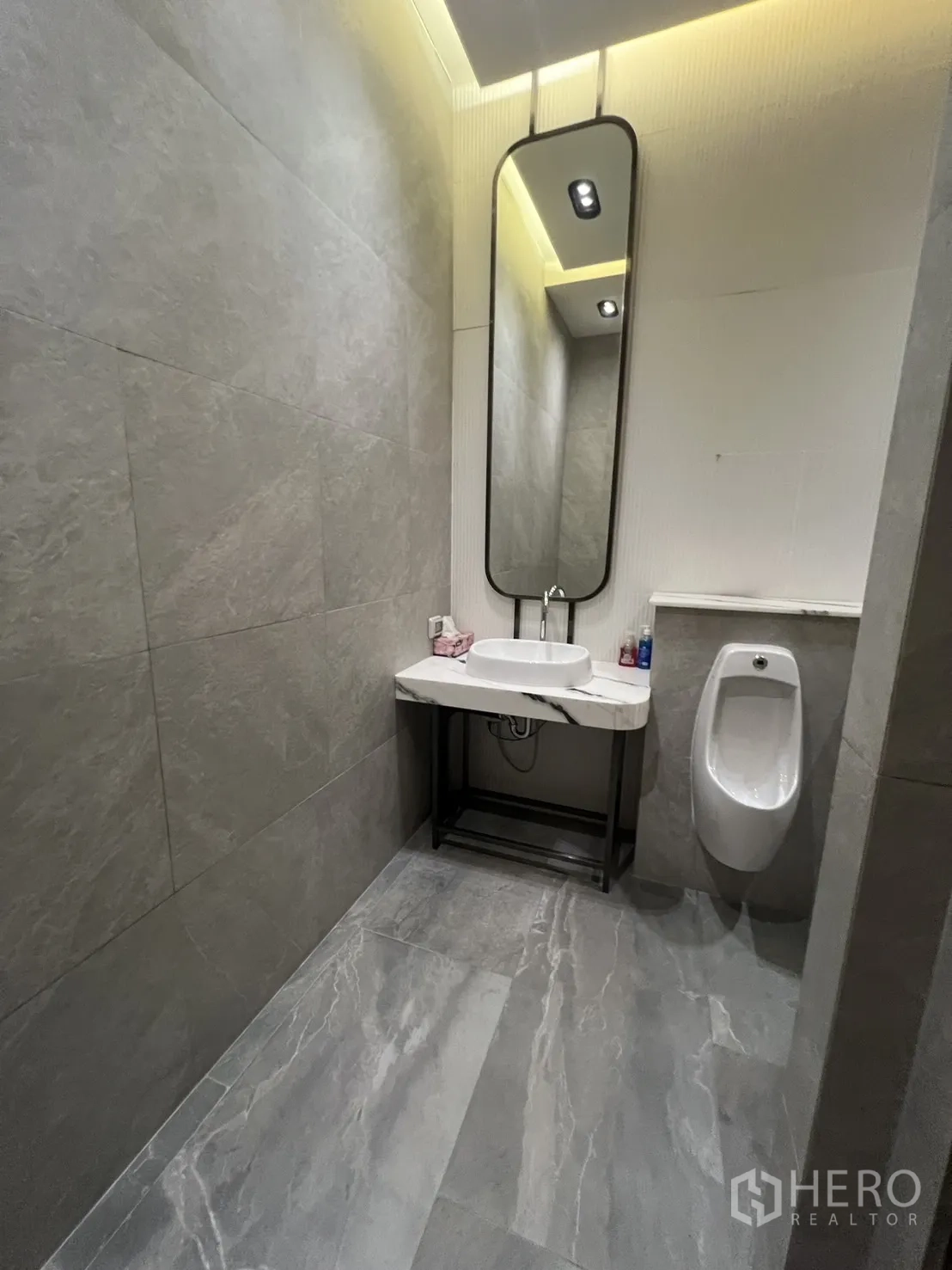 Retail Space for rent - Modern restroom with long mirror, basin, urinal and gray stone tiles.