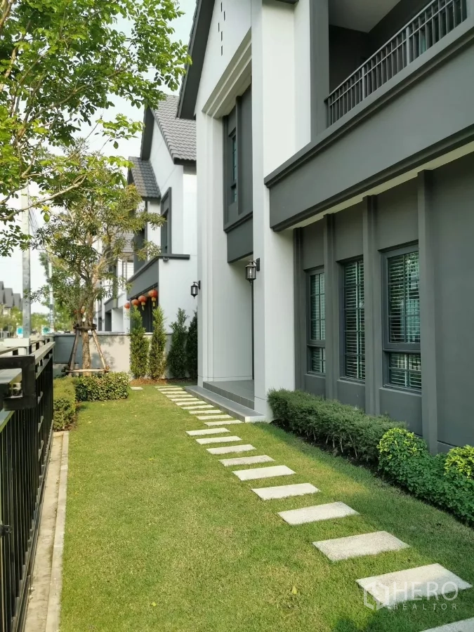 Detached House for rent in Bang Phli, Samut Prakan - Side garden with manicured lawn, stepping-stone path and tall windows along the facade.