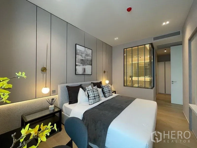 Condominium for rent in Watthana, Bangkok - Contemporary bedroom with a king bed, pendant lights, and a glass window to the ensuite bathroom.
