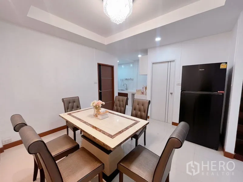 Townhouse for rent in Huai Khwang, Bangkok - Dining room with marble table, cushioned chairs, fridge and recessed lighting.