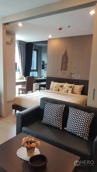 公寓 出租在Bang Rak, Bangkok - 一居室公寓的起居与卧室区，窗边书桌、沙发与抱枕。