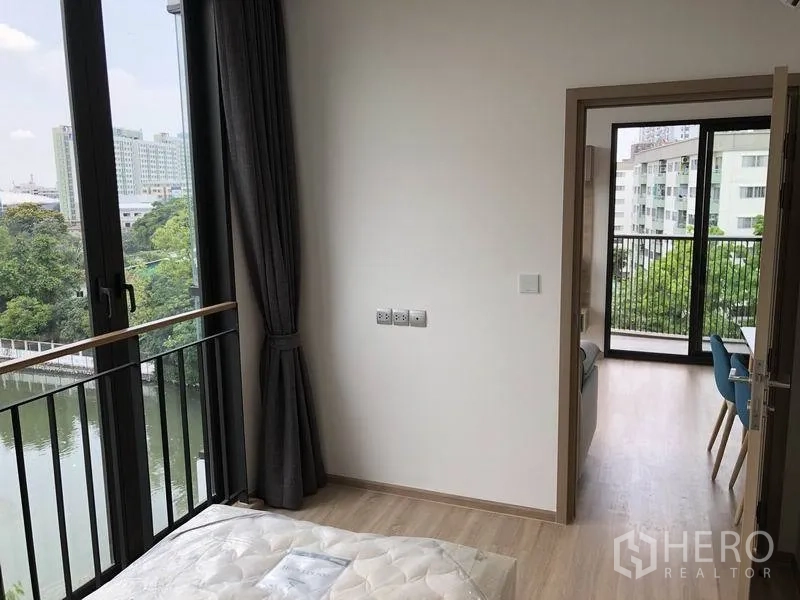 公寓 出租在Watthana, Bangkok - 卧室转角处的高窗与小阳台栏杆，可见运河与绿树，通向客餐厅。