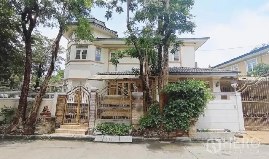 独立式住宅 出售在Bang Kapi, Bangkok - 两层独栋别墅外观，带铁艺大门与绿树围绕。