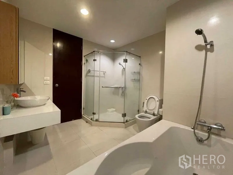 Condominium for rent in Din Daeng, Bangkok - Large bathroom with glass shower, bathtub, vanity and toilet in neutral tiles.