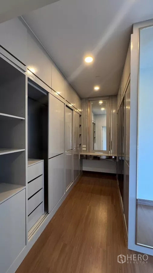 Detached House for rent or sale in Saphan Sung, Bangkok - Walk‑in closet corridor with full‑height built‑in cabinetry, drawers and vanity mirror over wood flooring.