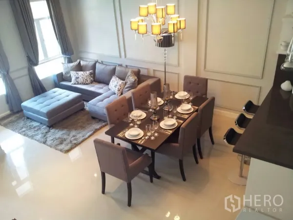 ทาวน์เฮาส์ ให้เช่าในWatthana, Bangkok - ห้องนั่งเล่นเชื่อมโซนทานอาหาร โซฟาสีเทา โคมไฟระย้า และโต๊ะทานอาหาร 6 ที่นั่ง