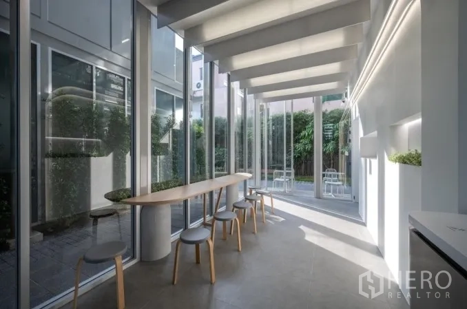 Retail Space for rent in Khlong Toei, Bangkok - Sunlit retail interior with a long wooden counter, stools, and floor-to-ceiling windows opening to greenery.