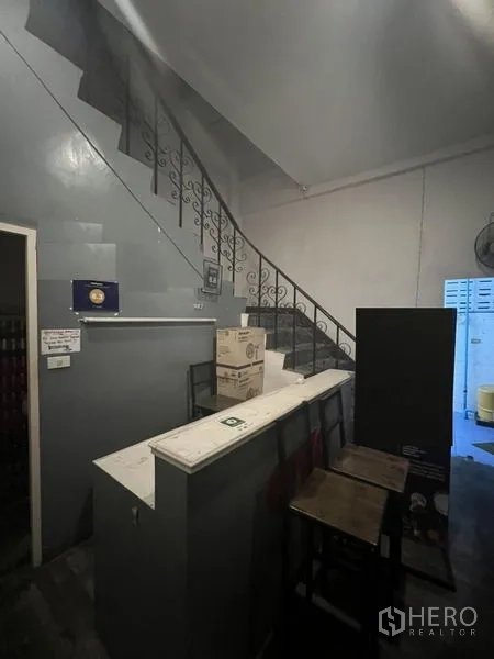 Shophouse for rent or sale in Watthana, Bangkok - Ground‑floor reception counter beside a staircase with wrought‑iron railing.