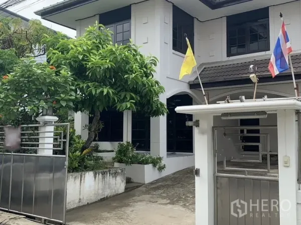Detached House for rent in Khlong Toei, Bangkok - Front exterior of a two-storey detached house with gated driveway and a mature tree.